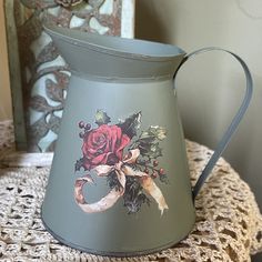 an old fashioned metal pitcher with roses painted on the side and ribbon around the handle