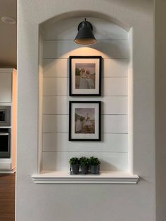 three framed pictures hang on the wall above a shelf with two potted plants in it