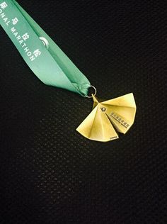 a gold medal with a green ribbon around it on a black surface, in the shape of a fan