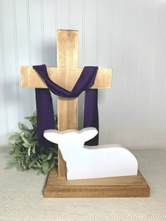 a wooden cross sitting on top of a table next to a purple cloth draped over it