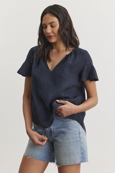 A person with long dark hair Fitted Linen Top For Casual Gatherings, Linen V-neck Tops With Ruffles, Effortless Linen V-neck Blouse, Relaxed Fit Linen Blouse With Ruffles, Casual Linen V-neck Blouse, Short Sleeve Linen Top With Ruffles, Relaxed Fit Linen Top With Ruffles, Linen Ruffled Short Sleeve Blouse, Linen Ruffled Short Sleeve Tops