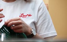 a woman is knitting while wearing a white t - shirt with the word lava on it