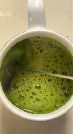 a green liquid in a white cup with a spoon