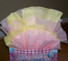 a pink and yellow baby shower gift bag with tissue paper in it on a wooden floor