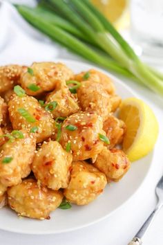 a white plate topped with fried chicken next to a lemon wedge and green onion garnish