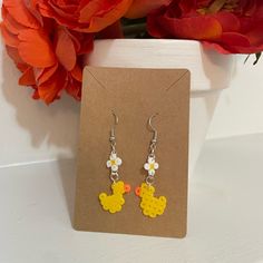 a pair of earrings with yellow and white flowers on them sitting next to a flower pot