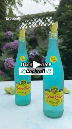 two bottles of ocean water sitting on top of a table next to lemon wedges