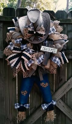 a cowboy hat wreath hanging on the side of a fence with blue jeans and boots