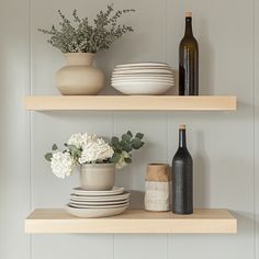 two shelves with plates, bowls and vases on top of each shelf in front of a wine bottle