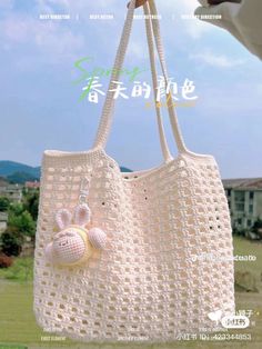 a white crocheted bag with two balls hanging from it's handle, in front of a blue sky