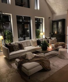 a living room filled with lots of furniture next to tall windows on top of a wooden floor