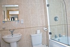 a white toilet sitting next to a bath tub under a bathroom mirror on top of a tiled wall