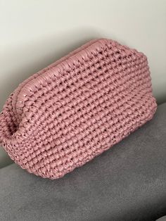 a pink crocheted purse sitting on top of a gray couch next to a white wall