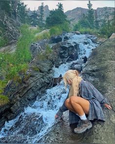 a woman sitting on top of a rock next to a waterfall