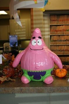 a pink inflatable character sitting on top of a counter next to pumpkins