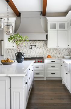 a large kitchen with white cabinets and wood flooring is pictured in this image, there are two vases on the island