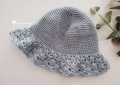 a crocheted hat with a bow on it next to some flowers and leaves