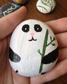 a hand holding a painted rock with a panda face and bamboo plant on it's side