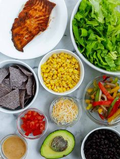 bowls filled with different types of food on top of a white countertop next to salads