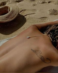 a woman laying on top of a sandy beach next to a hat and an umbrella