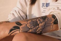 a woman's arm with a flower tattoo on it, sitting in front of a white wall