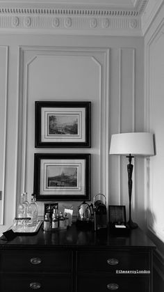 a black and white photo of a dresser in a room with pictures on the wall