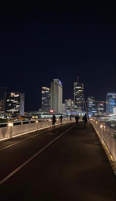 people walking across a bridge at night with city lights in the background