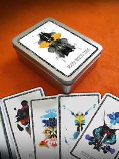 four playing cards in a tin sitting on a table next to each other with different designs