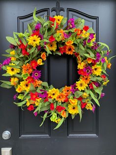 a colorful wreath is hanging on the front door with green leaves and red, yellow, purple, and orange flowers