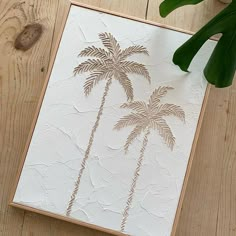 a painting with palm trees on it sitting on a wooden table next to a plant