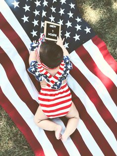 a baby sitting in front of an american flag holding up a sign that says it's now