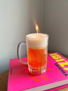 a lit candle sitting on top of a book next to a glass cup filled with liquid