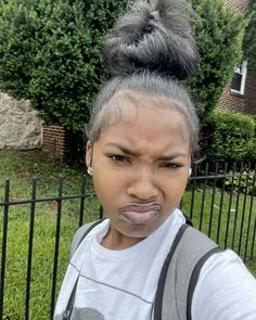 a woman with grey hair and suspenders making a funny face while standing in front of a fence