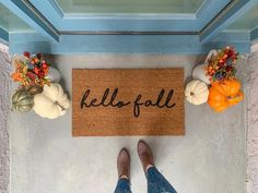 a person standing in front of a door mat with the word hello fall written on it