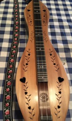 a wooden guitar is sitting on a checkered tablecloth with an embroidered band around the neck