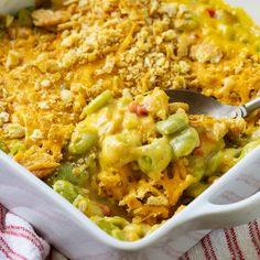 a casserole dish filled with green beans, cheese and other toppings next to a striped napkin