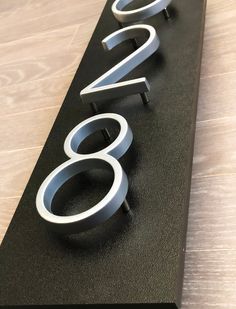 a black sign with silver numbers on it sitting on top of a wooden floor next to a wall