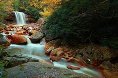 a small waterfall in the middle of a forest surrounded by rocks and trees with fall foliage around it