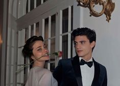 a man in a tuxedo standing next to a woman with a rose in her mouth