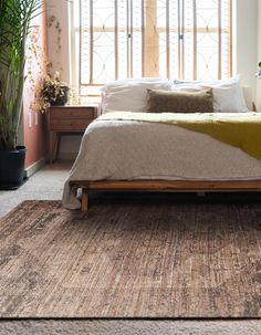 a bed sitting on top of a wooden floor next to a plant in a bedroom