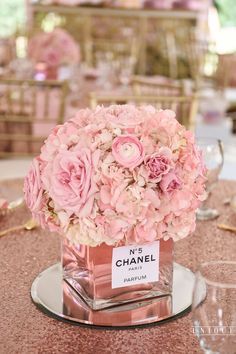 pink flowers in a square vase sitting on top of a table at a wedding reception