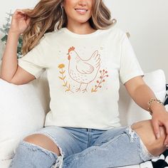 Embrace the charm of the countryside with our rustic chicken and flower shirt. Perfect for nature and animal lovers alike, this tee features a beautifully designed chicken amidst floral elements in a soft, inviting color palette. Made with high-quality materials, it offers both comfort and durability, making it a great addition to any wardrobe. Whether you're layering up for a brisk day or just showing off your love for farm animals, this T-shirt is sure to catch the eye and warm the heart. ☑️ P Country Style Short Sleeve T-shirt For Spring, Spring Country Style T-shirt With Graphic Print, Country Style Graphic Print T-shirt For Spring, Country Style Tops With Graphic Print For Spring, Country Style Graphic Print Tops For Spring, Relaxed Fit Country Tops For Spring, Relaxed Fit Country Style Tops For Spring, Country Style Relaxed Fit Tops For Spring, Chicken Graphic