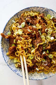 a bowl filled with noodles and meat on top of a white countertop next to chopsticks