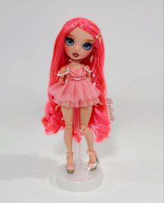 a doll with pink hair and blue eyes is standing on a white surface in front of a white background