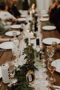 the table is set with white plates and wine glasses, candles, and greenery