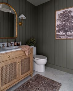 a white toilet sitting next to a bathroom sink under a large framed painting on the wall