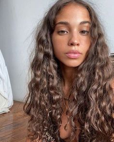 a woman with long curly hair is sitting on the floor and looking at the camera