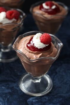 three desserts with raspberries and whipped cream in small glasses on a blue cloth