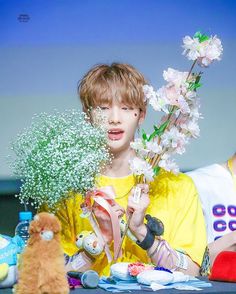 a boy with flowers in his hand and stuffed animals around him on the table next to him