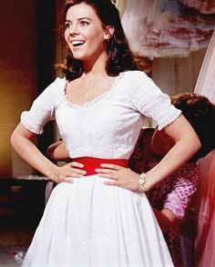 a woman in a white dress is standing with her hands on her hips and smiling